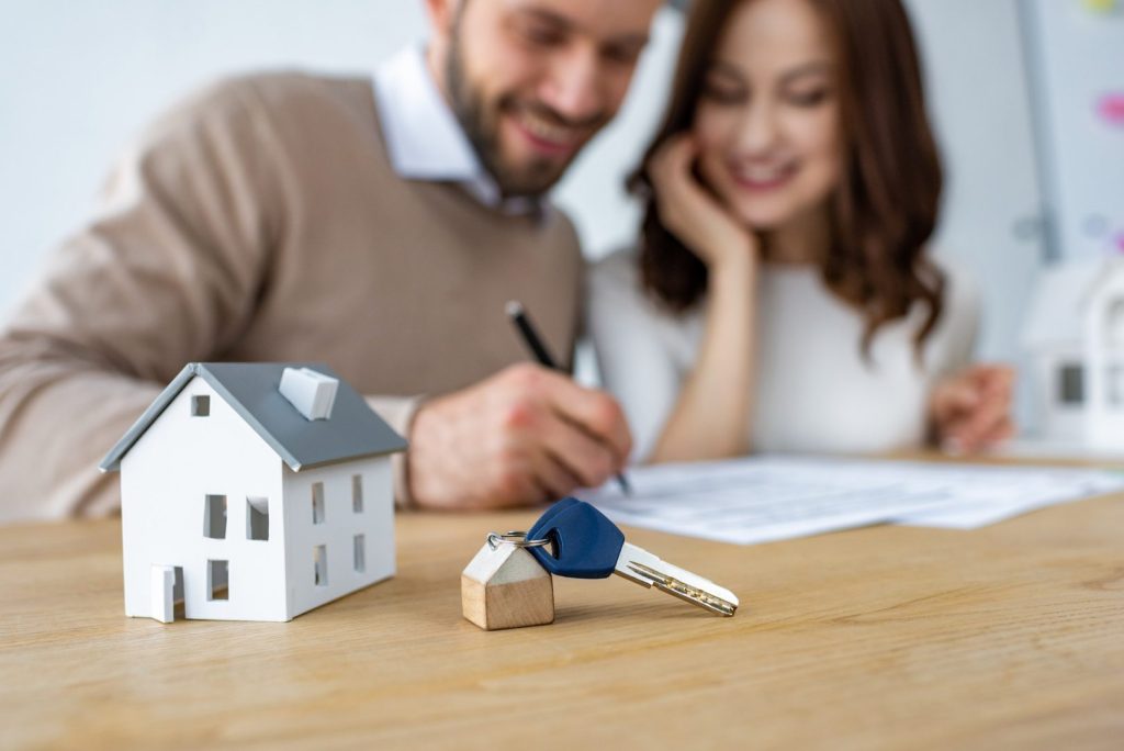 selective focus of house model and keys near happy man and woman